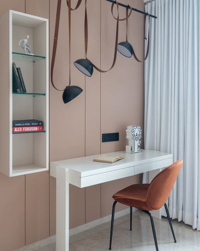 White desk with rust velvet chair under sculptural pendant lamps against dusty pink panelled wall