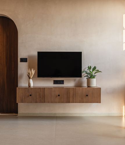Floating fluted wood console under wall-mounted TV beside an arched walnut door in a minimal living room