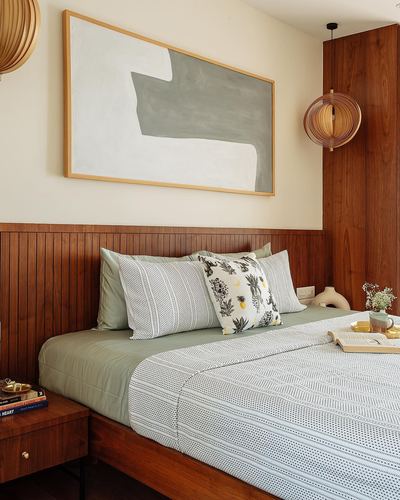 Bedroom with ribbed wood headboard wall, abstract art, and sage green bedding under pendant light