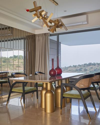 Dining table with brass cylinder base and cane chairs under sculptural wood chandelier, hill view beyond