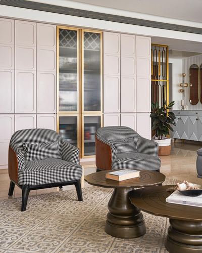 Living room with houndstooth armchairs, brass pedestal coffee tables, and a blush paneled wall with gold-trimmed cabinet
