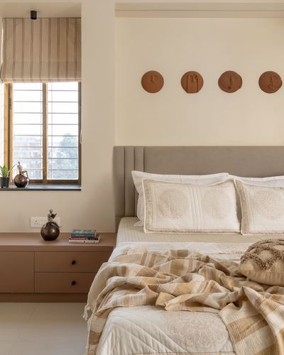 Bedroom with grey headboard, terracotta wall discs, striped blind and layered plaid throw