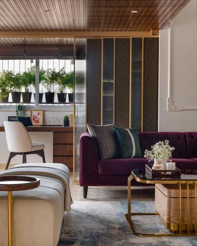 Living room with plum velvet sofa, brass coffee table, and fluted glass partition beside a wooden desk