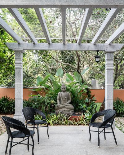 Stone pergola over patio with black woven chairs facing a garden buddha statue