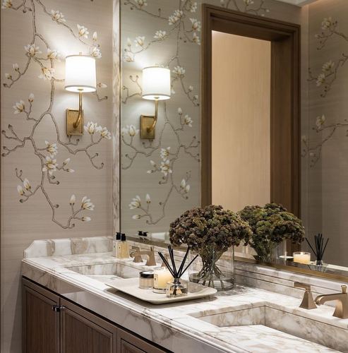 Marble double vanity beneath floral wallpaper with brass sconces and mirror reflection