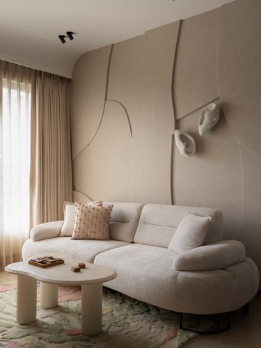 Curved cream boucle sofa against sculptural plaster wall with organic sconces in Mumbai living room