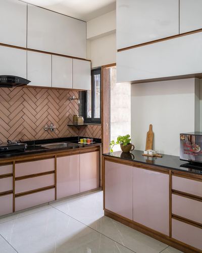 Pink glossy kitchen cabinetry with terracotta herringbone backsplash and black stone countertop