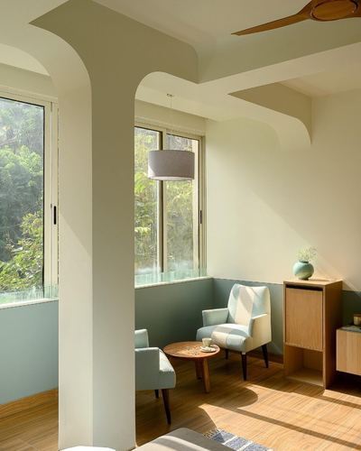 Sunlit living nook with sage half-walls, sculpted arched ceiling column, and patterned armchairs