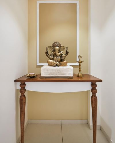 Brass Ganesha idol on a wooden console table with mirror above, in a beige alcove