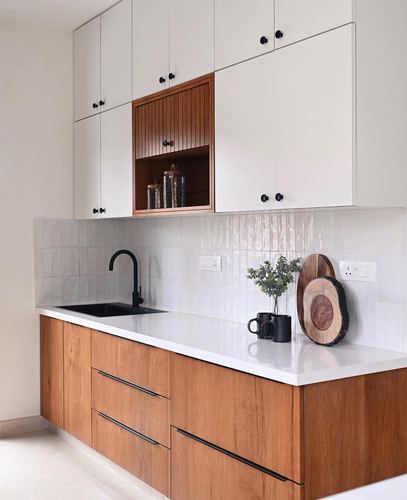 Modern galley kitchen with white upper cabinets, wood lower units, and black hardware