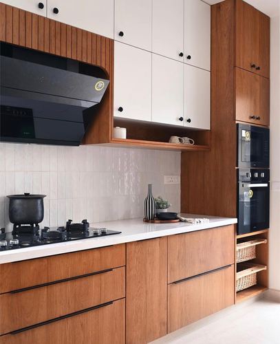 Modern galley kitchen with wood cabinetry, white counters, black hob and built-in ovens