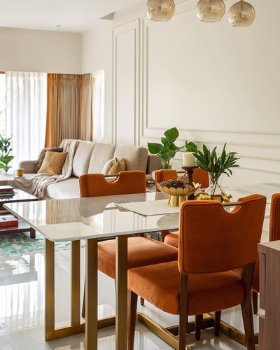 Dining area with glass-top brass table, orange velvet chairs, and living room beyond