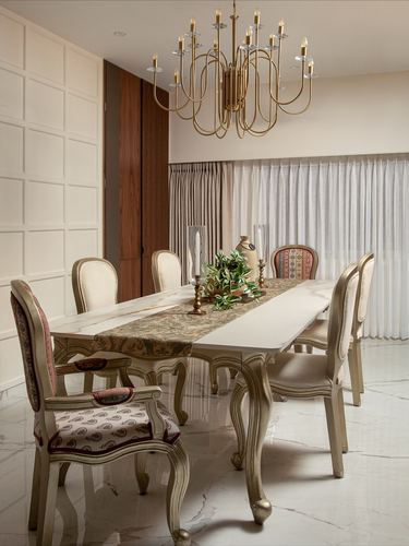 Formal dining room with marble table, carved cream chairs, and brass candelabra chandelier
