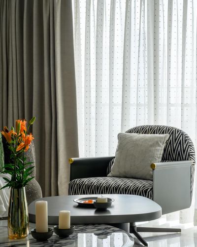Zebra-print armchair by sheer curtains with dark round coffee table and orange lilies