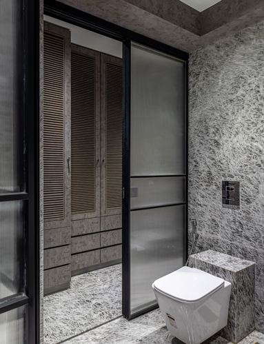 Grey stone bathroom with black-framed fluted glass sliding door and louvered wardrobe beyond