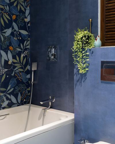 Blue bathroom with floral wallpaper accent wall, white bathtub, and hanging plant near shuttered window