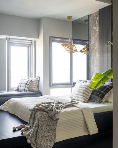 Bedroom with grey stone wall, brass geometric pendant, window seat, and layered neutral bedding