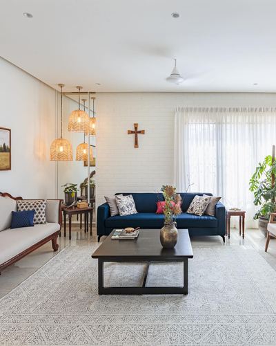 Living room with navy sofa, white brick accent wall, wooden cross, and cane pendant lights over a mirrored console