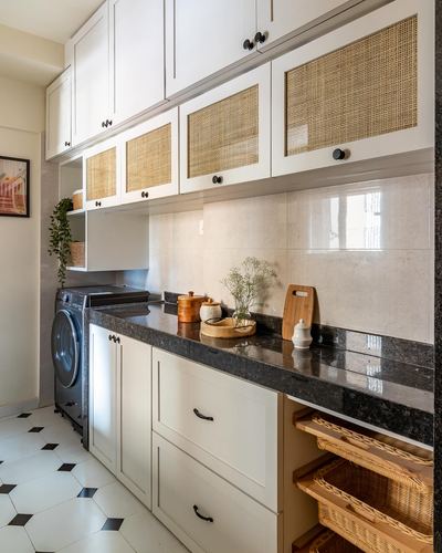 Galley kitchen with white cabinetry, cane-front uppers, dark stone counter, and washing machine below.