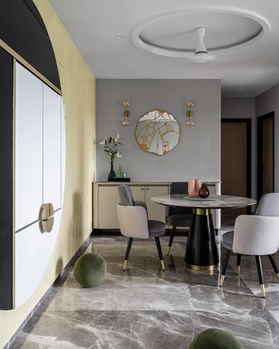 Dining area with round marble table, houndstooth chairs, and sunburst wall art in a Mumbai apartment