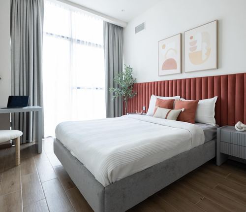 Bedroom with terracotta channel-tufted headboard, grey bed, wood floor, and daylight through sheer curtains