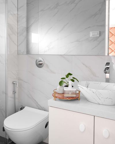 Minimalist white marble-look bathroom with vessel sink, wall-hung toilet, and blush accent tray