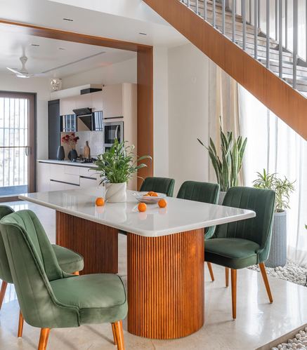 Dining table with fluted wood base, green velvet chairs, staircase and kitchen beyond