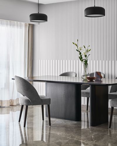 Dining room with dark wood table, grey upholstered chairs, fluted white wall panels, and black pendant lights