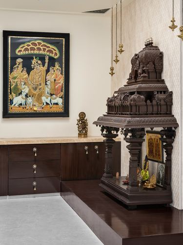 Carved wooden pooja mandir beside tanjore painting in a traditional Chennai home shrine room
