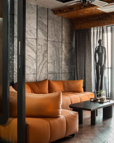 Living room with orange leather sofa, stone-clad wall, wood ceiling and standing figurative sculpture