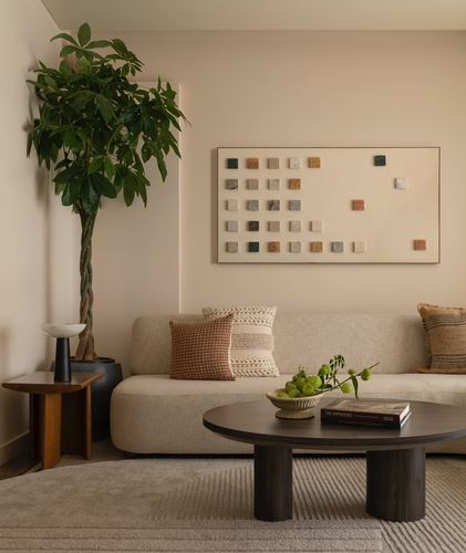 Beige living room with curved sofa, round dark wood coffee table, and tall potted plant