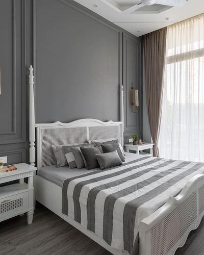 White cane four-poster bed against grey paneled wall with striped grey bedding