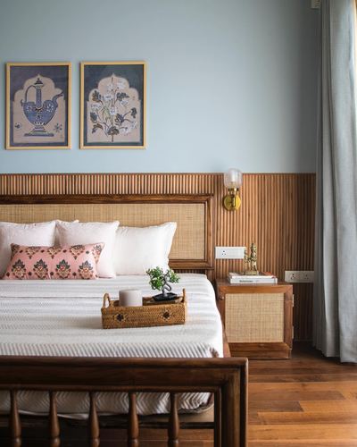 Bedroom with cane headboard, fluted wood wall panelling, powder blue walls, and framed miniature art