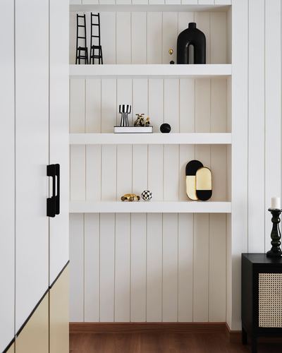 White vertical-panelled shelving niche with black and gold decor objects beside a black cane cabinet