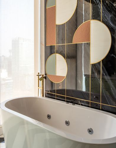 Freestanding tub beneath black marble wall with gold-lined geometric mirror panel and city view window