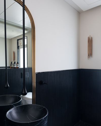 Bathroom corner with black marble vessel sinks, brass arched mirror, and ribbed black wainscoting.