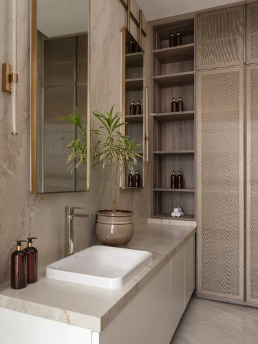 Bathroom vanity with stone countertop, brass-framed mirrors, wood shelving, and woven-pattern wardrobe front.