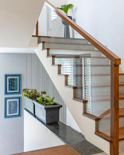 Wooden staircase with glass balustrade beside grey paneled wall and blue framed art