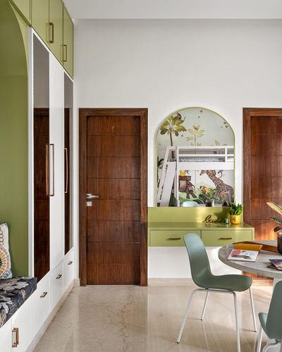 Green wardrobe wall, wooden doors, and an arched jungle mural above a floating study desk with round table and chairs