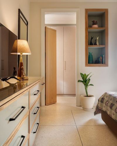 Bedroom hallway with terrazzo floor, wooden door, dresser, and a niche shelf displaying decor objects