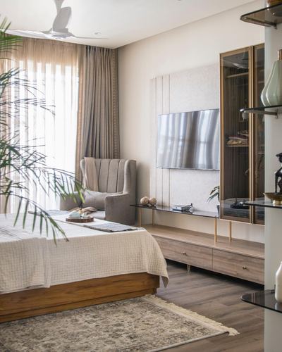 Bedroom with wooden bed, wingback chair, and paneled TV unit beside glass display cabinet