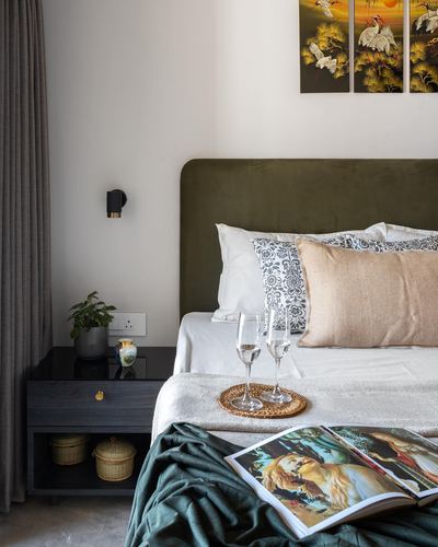Bedroom with arched olive velvet headboard, patterned pillows, dark wood nightstand and bird-motif wall art