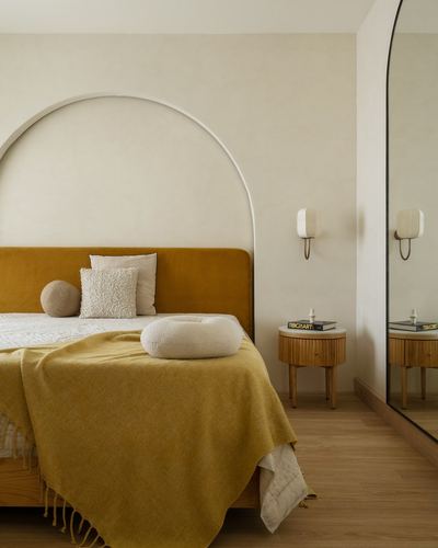Bedroom with mustard velvet headboard against arched plaster niche and wooden bedside table