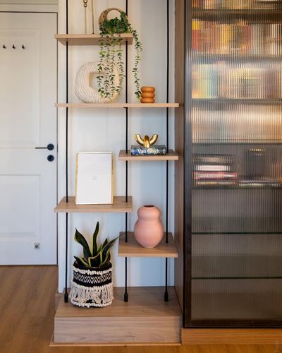 Staggered wooden floating shelves styled with plants and ceramics beside a ribbed glass cabinet door