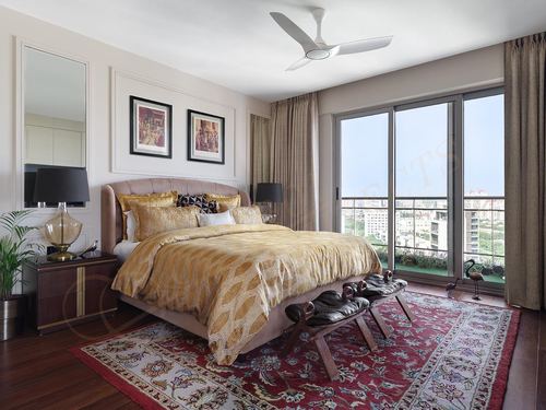 Luxurious bedroom with gold bedding, tufted headboard, patterned rug, and city-view balcony