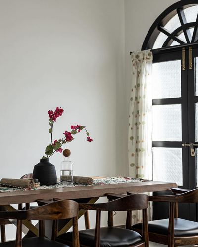 Dining table with black vase of bougainvillea beside an arched black-framed patterned glass door