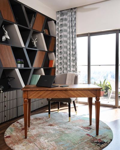 Wooden desk with laptop in front of geometric bookshelf, large window with city view behind
