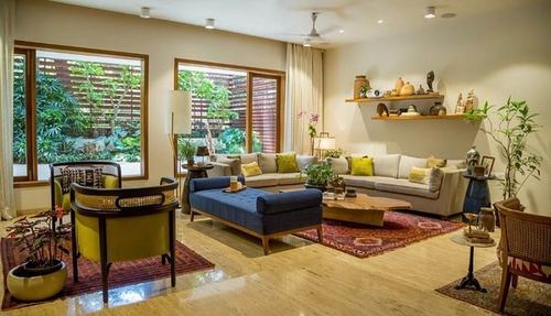 Living room with beige sectional, blue ottoman, wooden coffee table and large windows to garden