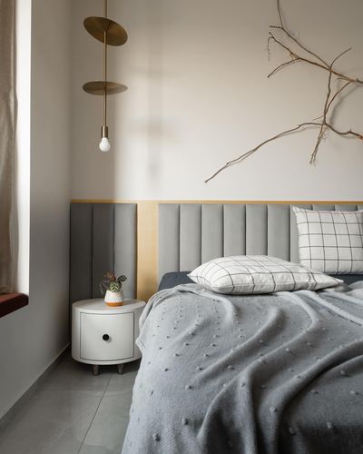 Grey channel-tufted headboard bed with round white nightstand and brass disc pendant light