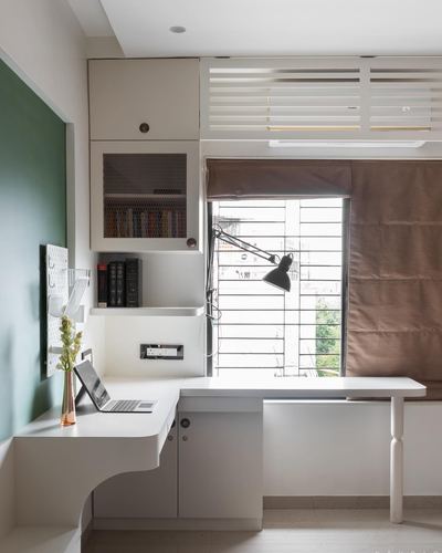 White corner study desk with black task lamp beneath a window, green accent wall beside cabinetry